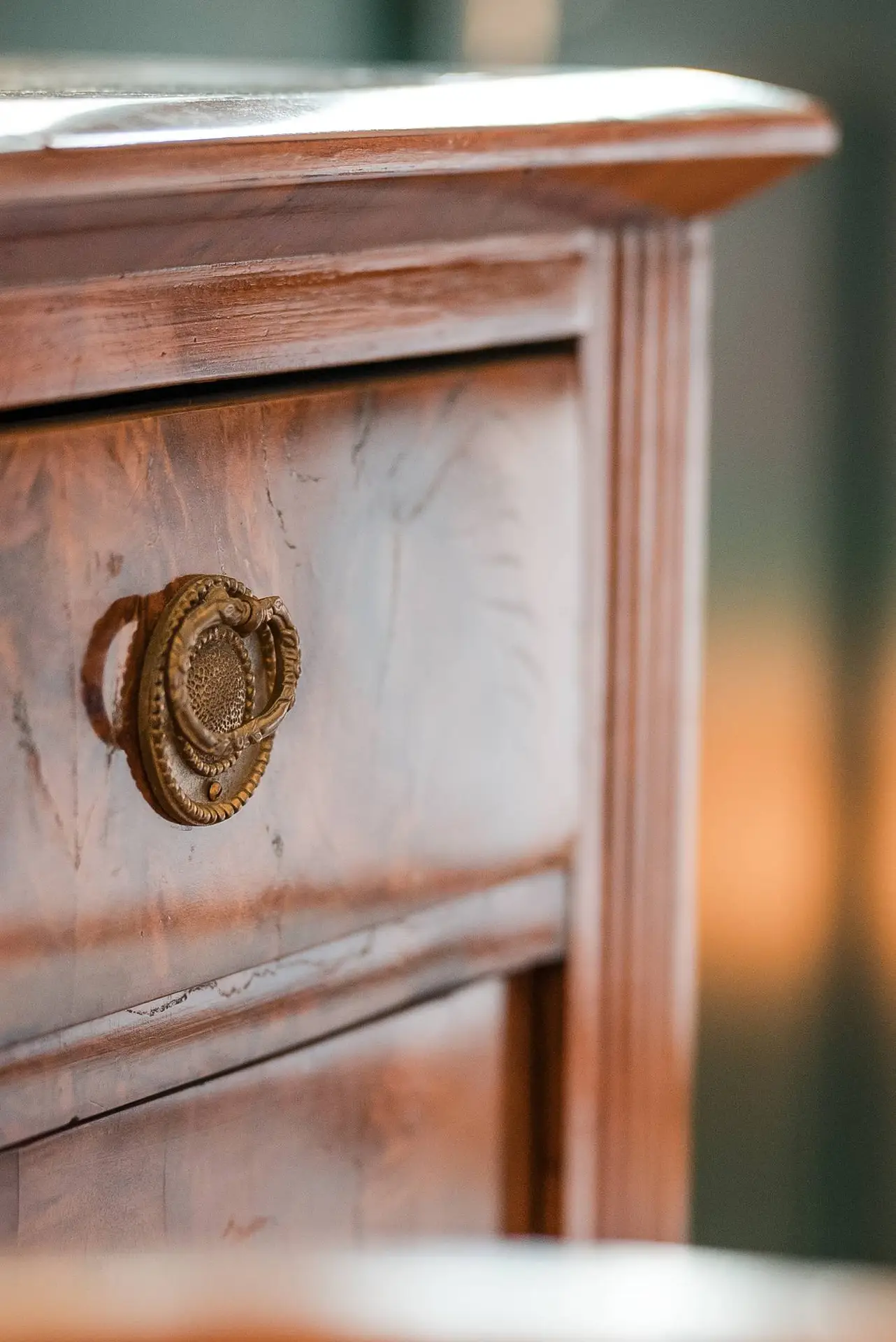 Nahaufnahme eines verzierten Schubladengriffs aus Messing an einer Vintage-Kommode aus Holz mit detaillierter Holzmaserung vor weichgezeichnetem Hintergrund.