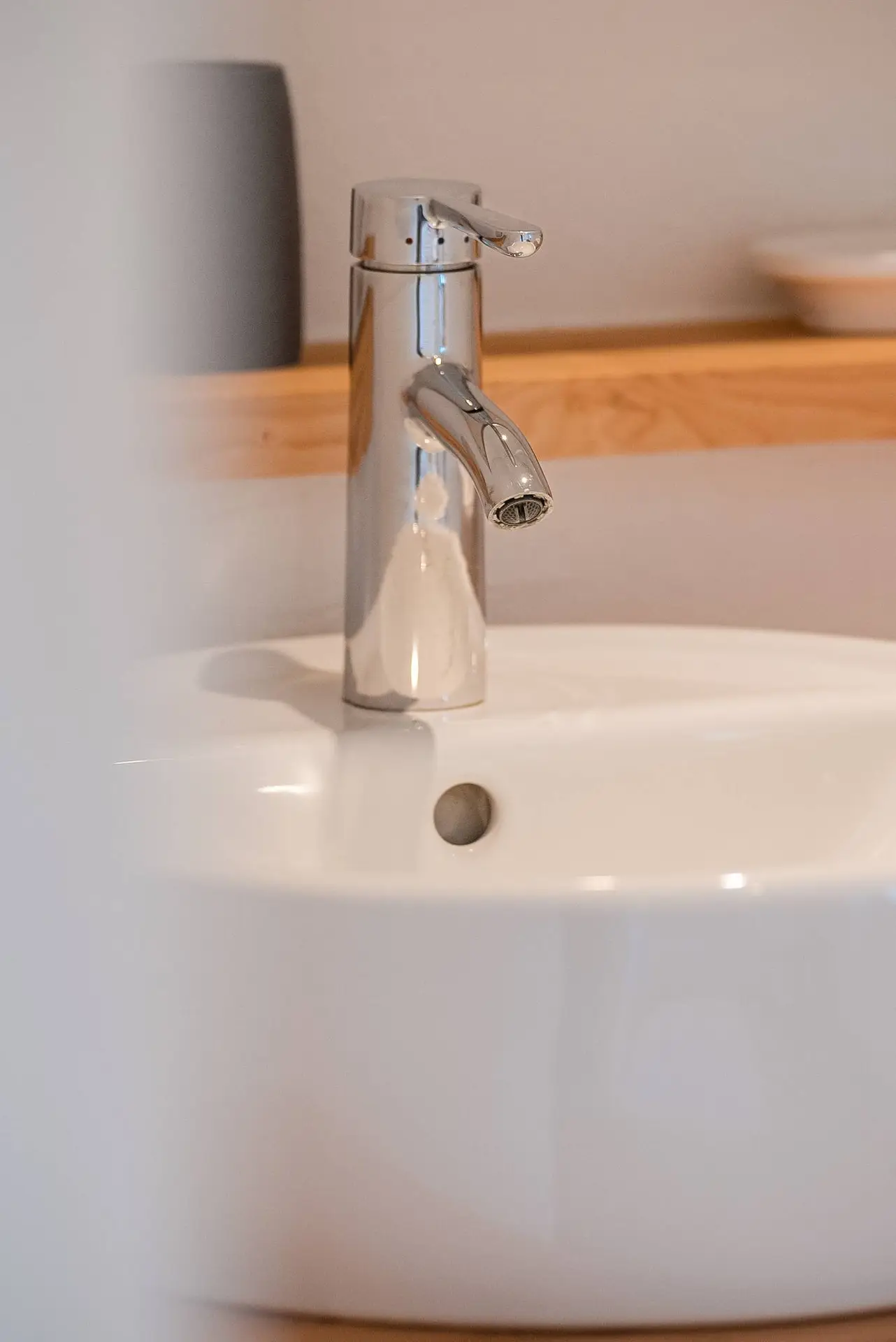 Ein moderner Chromhahn über einem weißen Badezimmerwaschbecken, mit weichem Fokus auf einem neutral getönten Hintergrund.