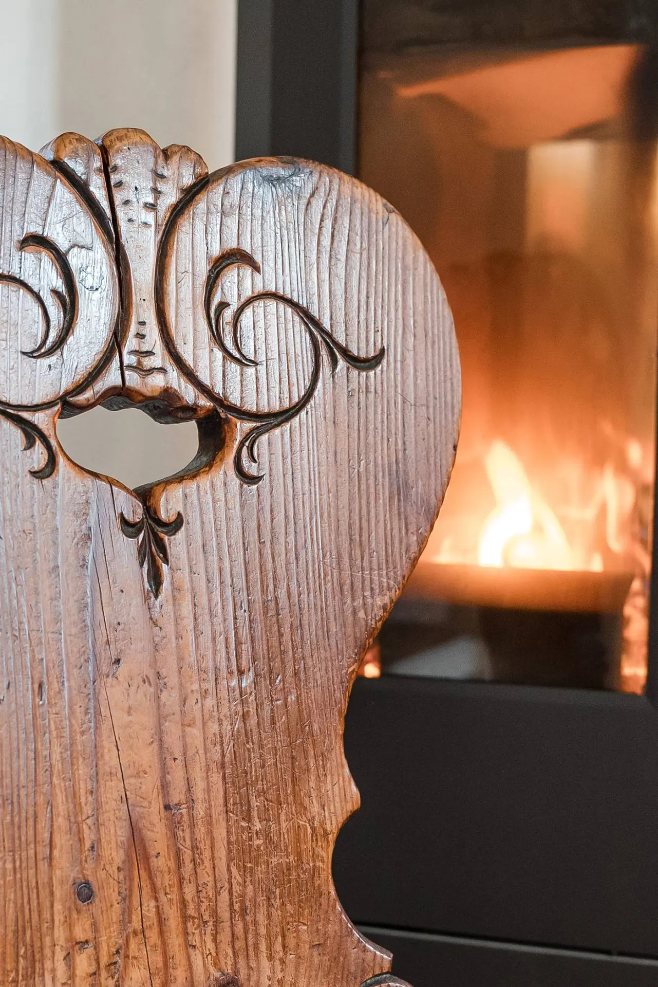 Nahaufnahme einer kunstvoll geschnitzten Stuhllehne aus Holz mit einem unscharfen Kamin im Hintergrund.